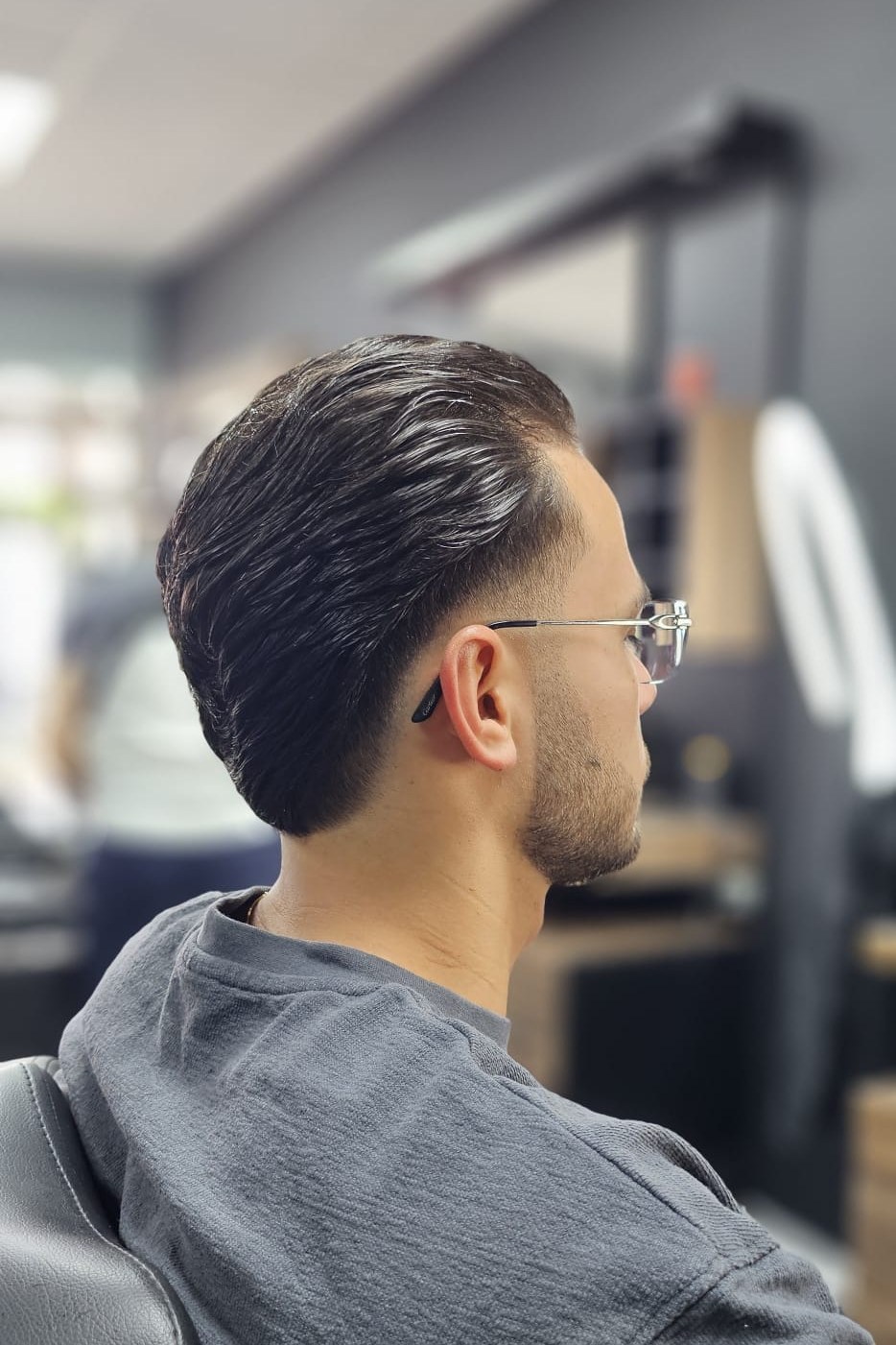 Zijaanzicht van een klant met een strak geknipt, naar achteren gekamd kapsel en een korte baard